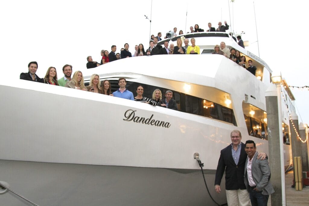FSY Corporate Events – Gallery (46) Large group posed on the upper deck and bow of the yacht Dandeana with its name lettered on the hull