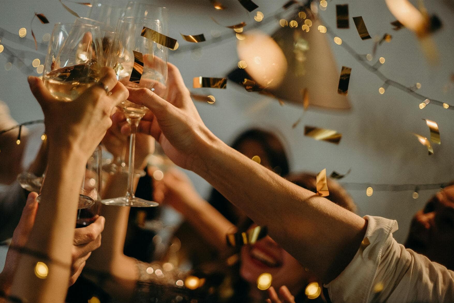 Celebration - hand holding champagne glasses in the air, gold confetti.